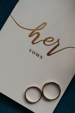 Wedding vows booklet with elegant gold lettering and two gold wedding bands displayed on a dark background.