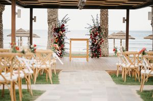 Elegant beach wedding ceremony setup with floral arch and wooden chairs overlooking the ocean.