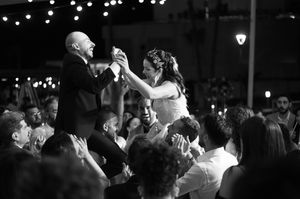 A black and white photo shows two dancers being lifted during a celebration by a crowd at a formal event.