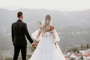 A couple in wedding attire holding hands while overlooking a scenic mountain landscape at sunset.
