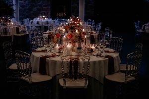 An elegant wedding reception table setting with glowing red candlelight centerpieces and silver chiavari chairs.