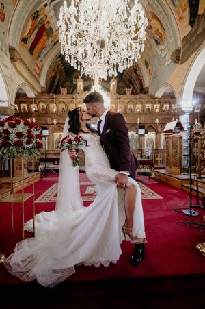 Romantic dance dip pose in an ornate ballroom with crystal chandeliers and red carpet.