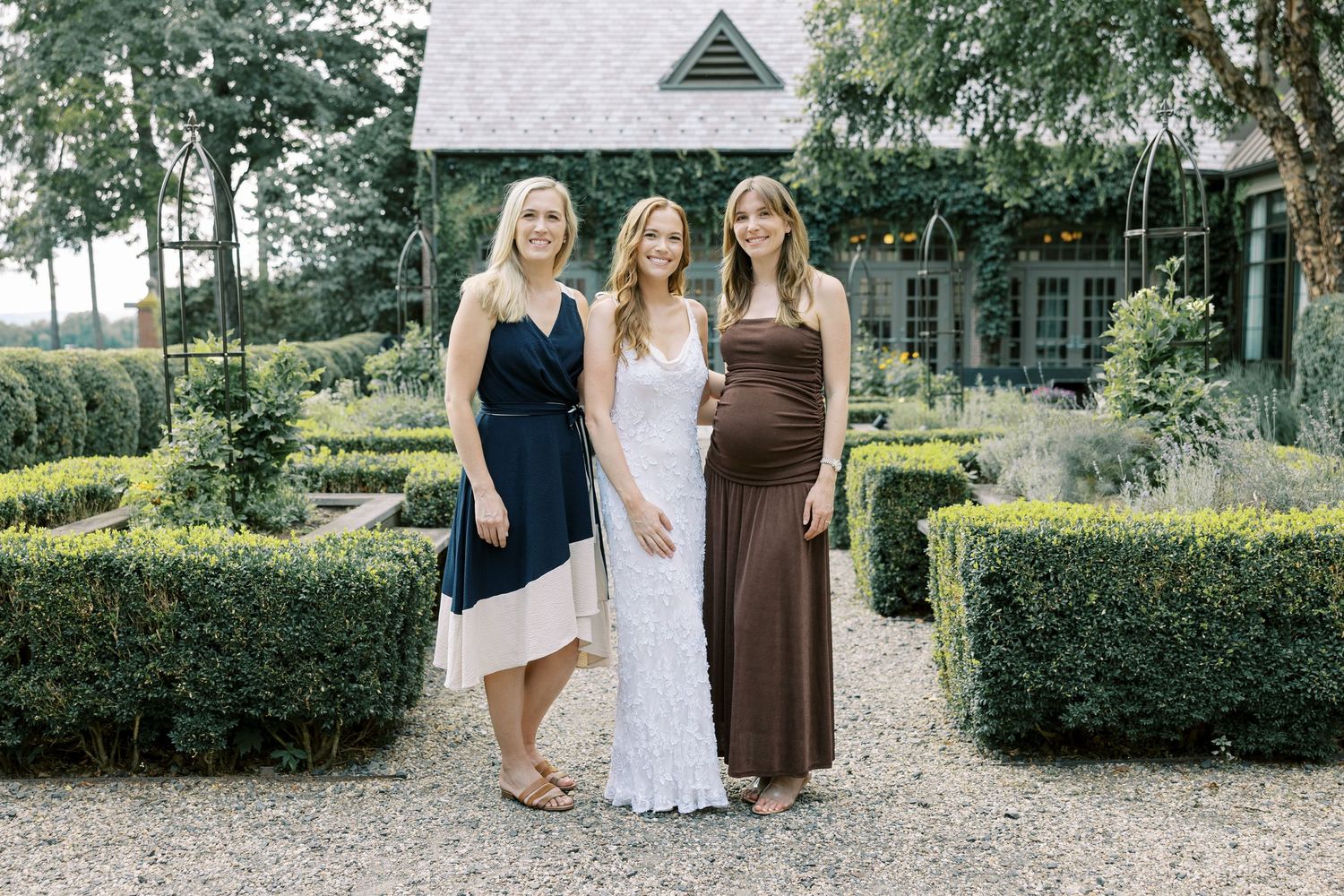 Three people stand together in a manicured garden setting surrounded by neatly trimmed hedges and greenery at Ninety Acres.