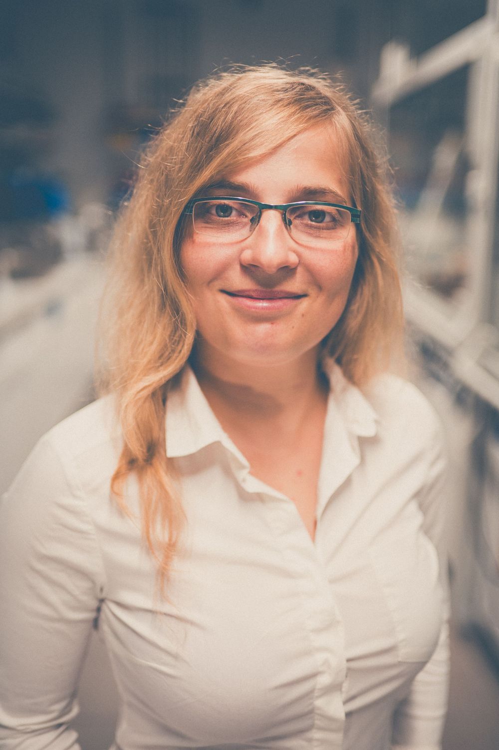 Professional portrait of a person wearing glasses and a white button-up shirt, with soft lighting and warm tones.