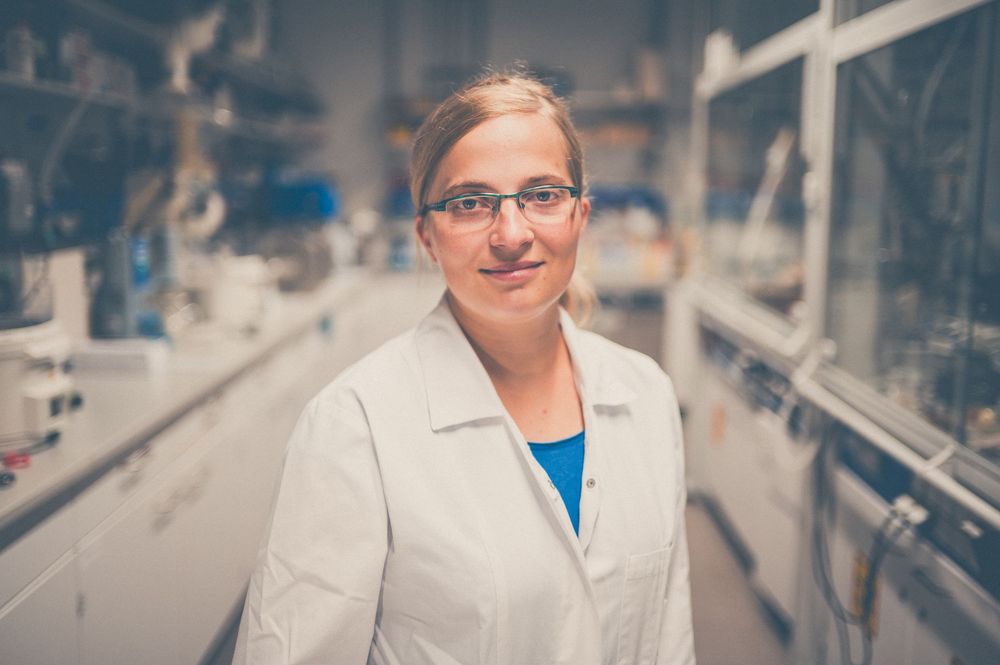 Scientist in laboratory coat examines clear liquid samples in test tubes for medical research purposes.