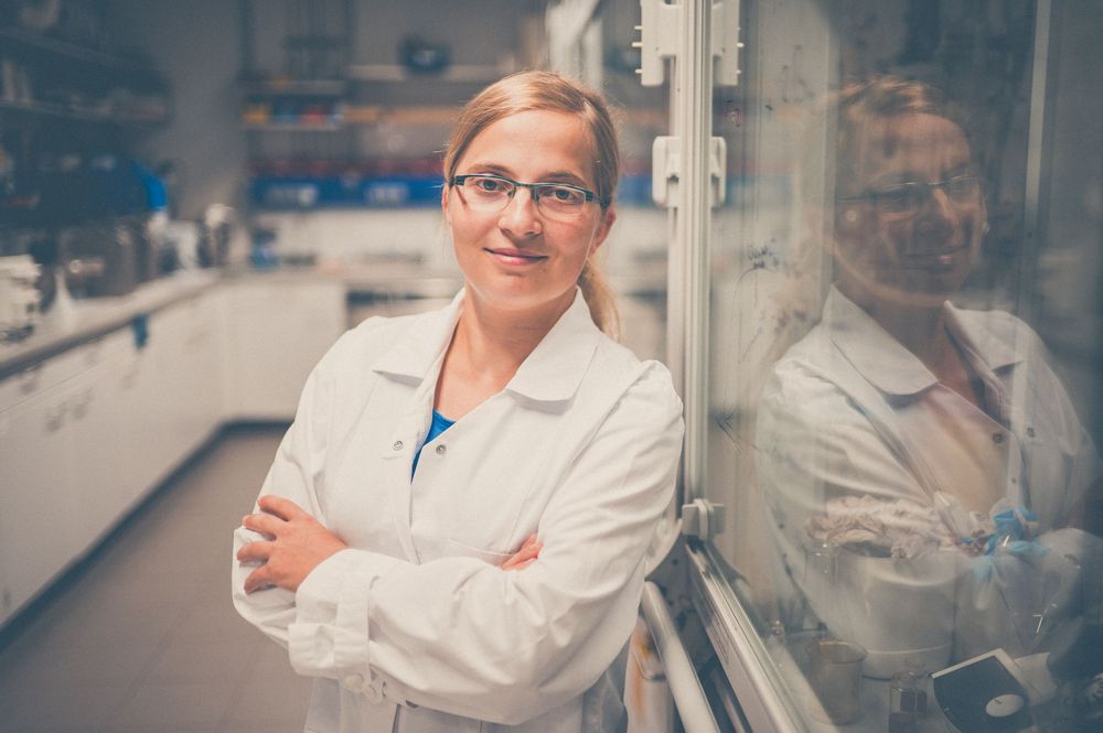 A medical professional in a white lab coat stands with arms crossed in a laboratory setting.