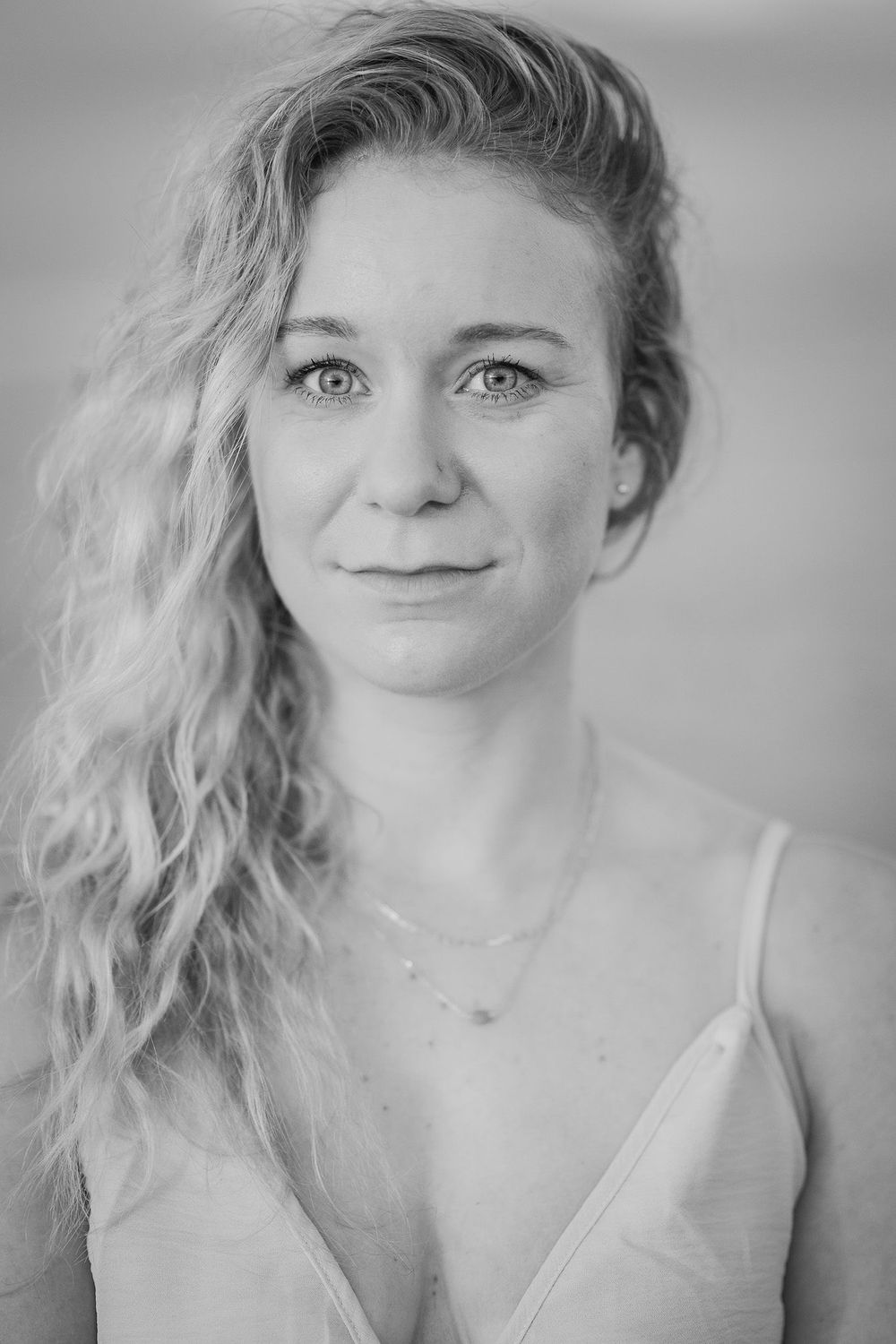 Black and white portrait with soft lighting showing wavy blonde hair, delicate necklace and white top in intimate style.