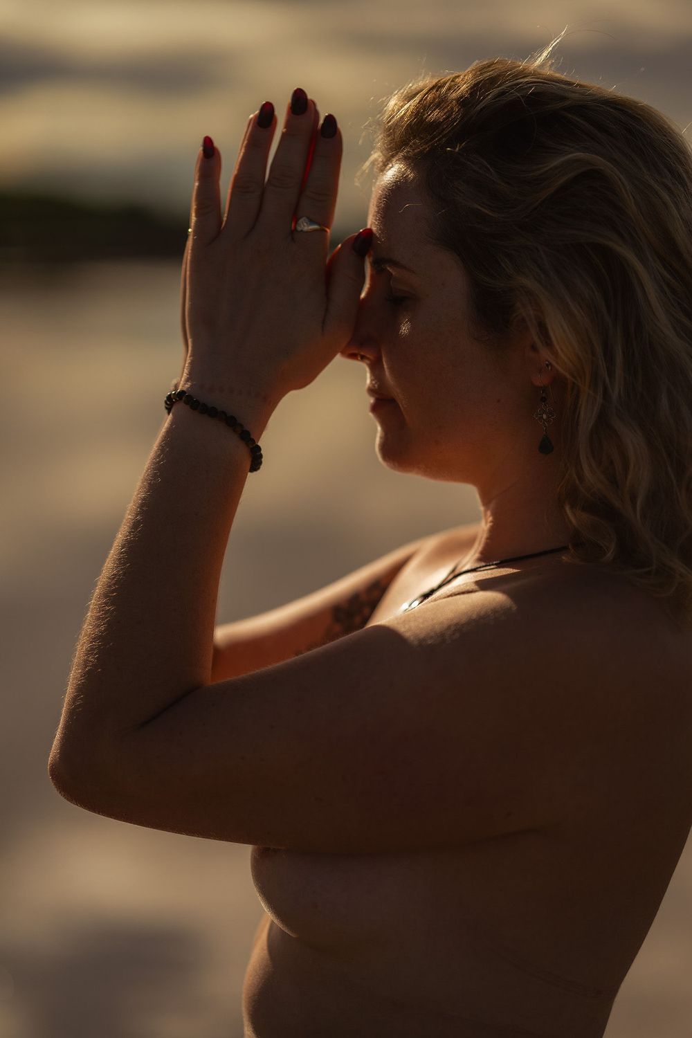 Silhouette of a person shielding their eyes from golden sunlight during sunset or sunrise in warm tones.