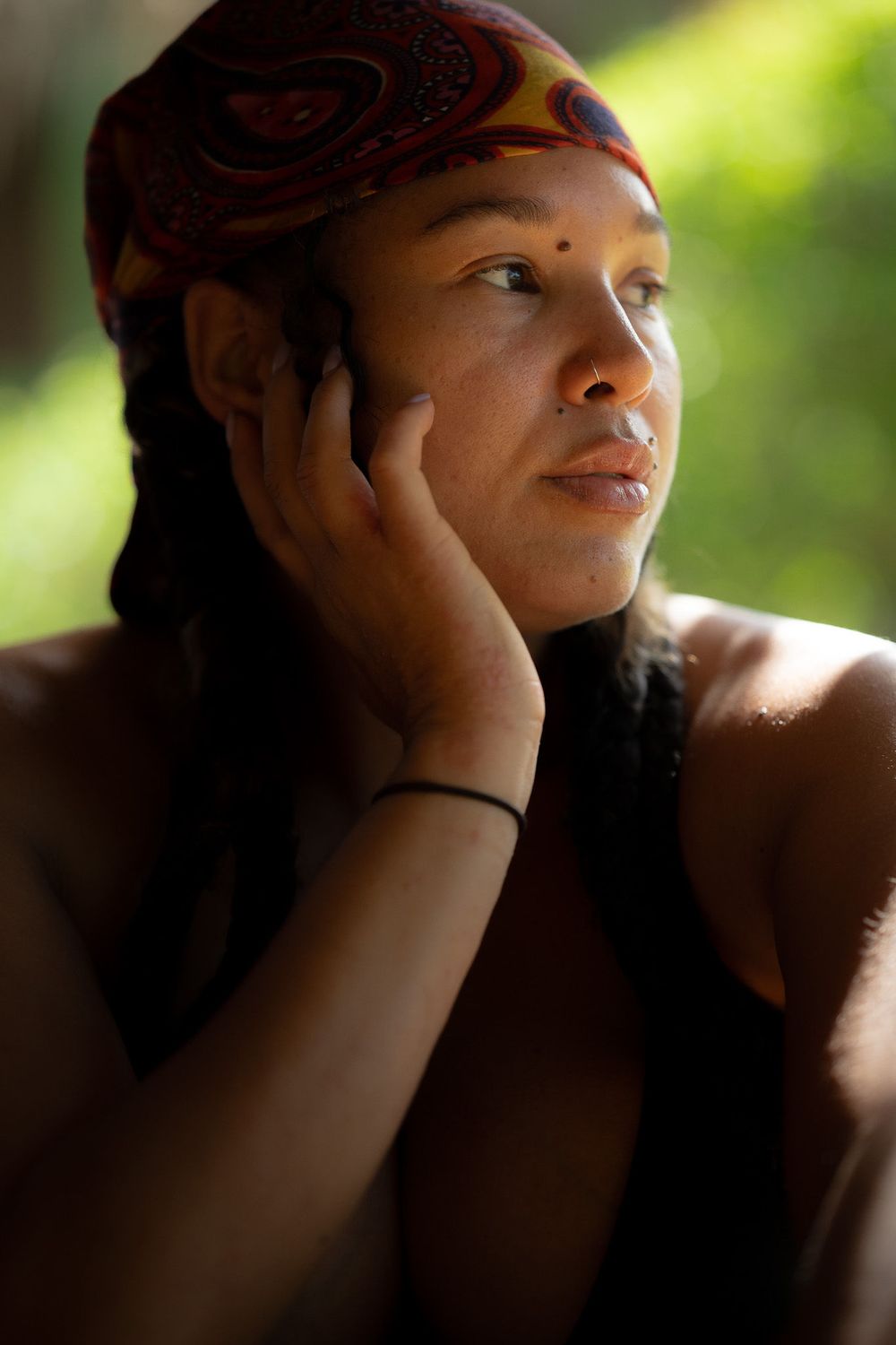 Person wearing a brown patterned headband gazes contemplatively while resting their head on their hand in soft lighting.