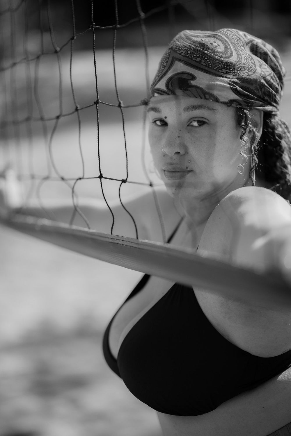 Black and white artistic volleyball player looking through net during beach volleyball match.