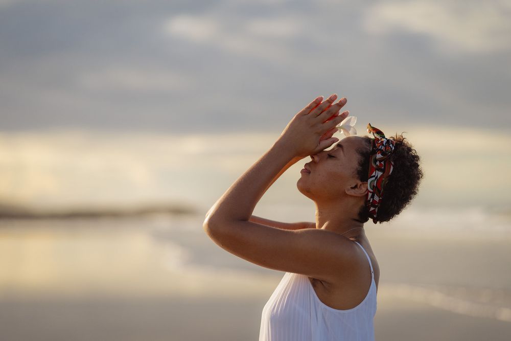 A person takes a refreshing sip of cold beverage while walking along a beach at sunset.