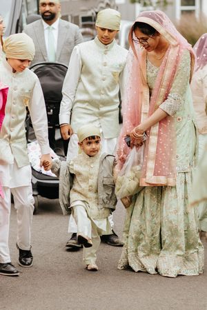 A traditional South Asian wedding party wearing elegant cream and pastel colored formal attire walking together outdoors.