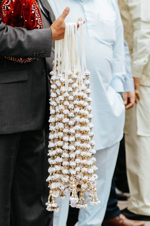 Traditional decorative garland made of small white bells and ribbons held against formal attire.