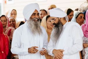 A group of people in traditional Sikh attire gather together at a religious ceremony wearing white garments.