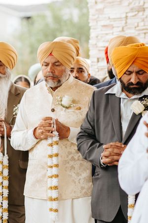 Several men in traditional Sikh attire with orange turbans and formal wear gather during a ceremony.