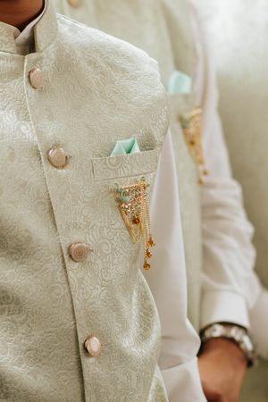 Close-up detail of a mint green brocade wedding sherwani with fabric-covered buttons and ornate pocket detail.