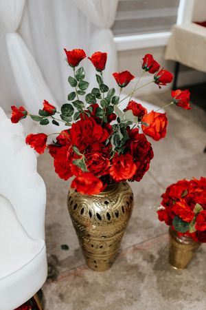 Vibrant red roses arranged in an ornate gold vase against a white background.