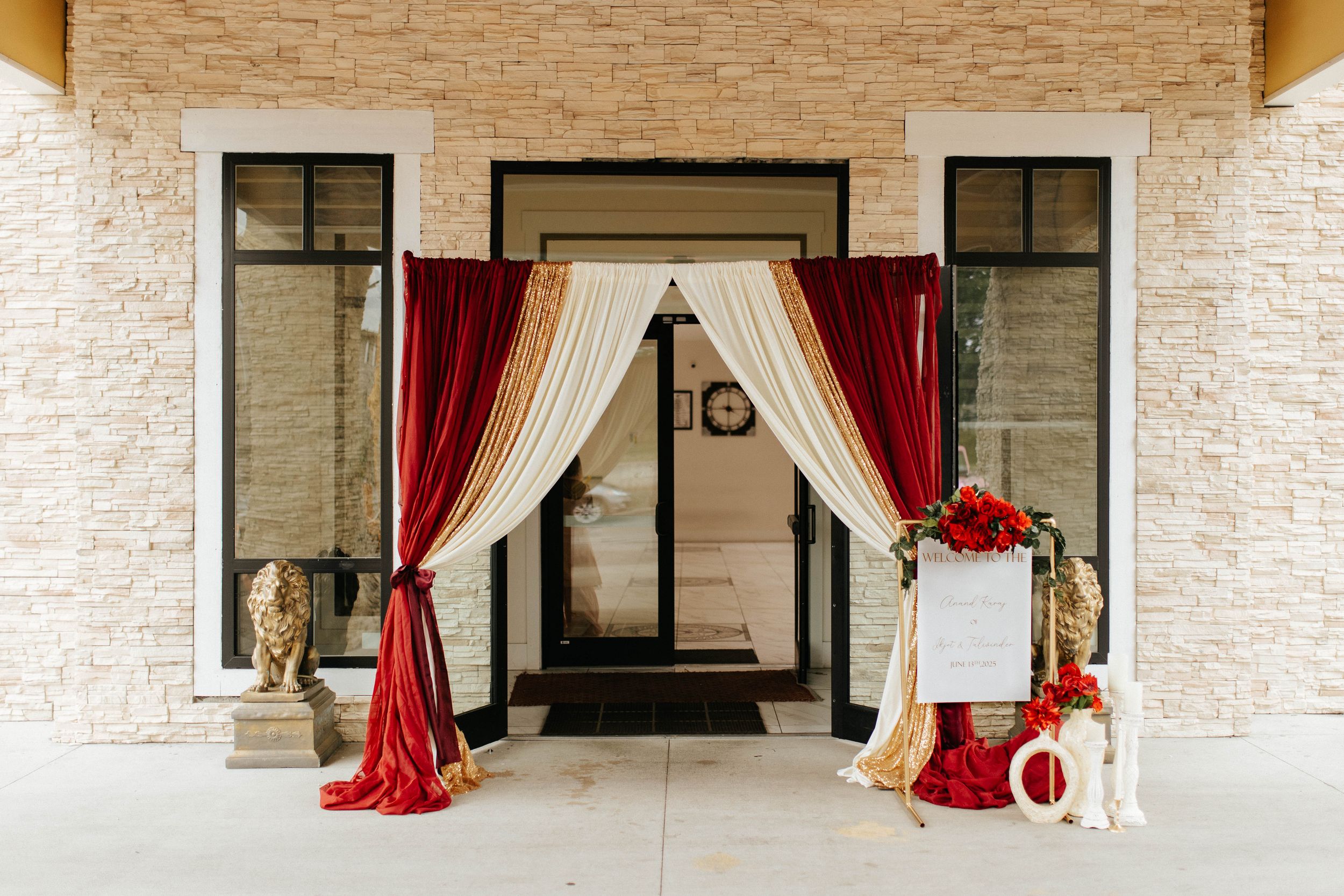 Elegant wedding arch entrance with red and cream curtains draped between gold pillars against a white stone wall.