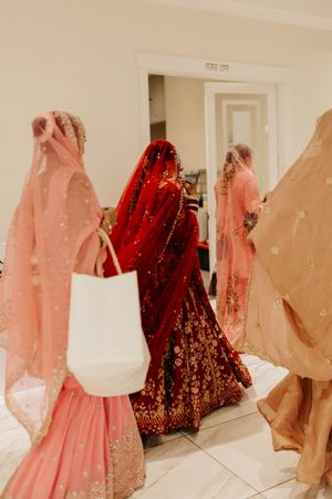 A row of pink and red bridal lehengas and dresses hanging on display in a bright white dressing room.