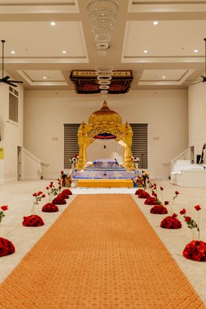 Ceremonial hall with orange carpet runner leading to golden canopy and crystal chandelier.