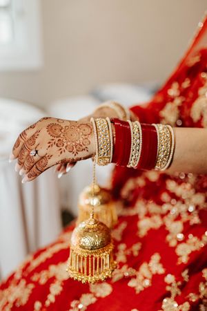 Ornate golden bangles and jewelry displayed with traditional henna-adorned hands against red fabric.