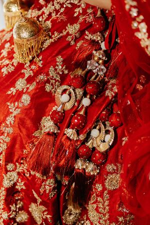 Intricate red and gold embroidered fabric with traditional ornate details and tassels in rich crimson colors.