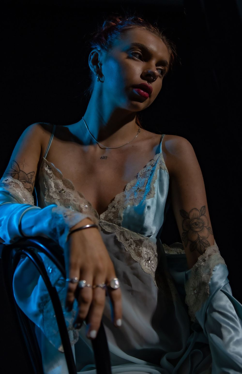 Artistic portrait lit with blue tint showing close-up details of jewelry and lace against dark background.