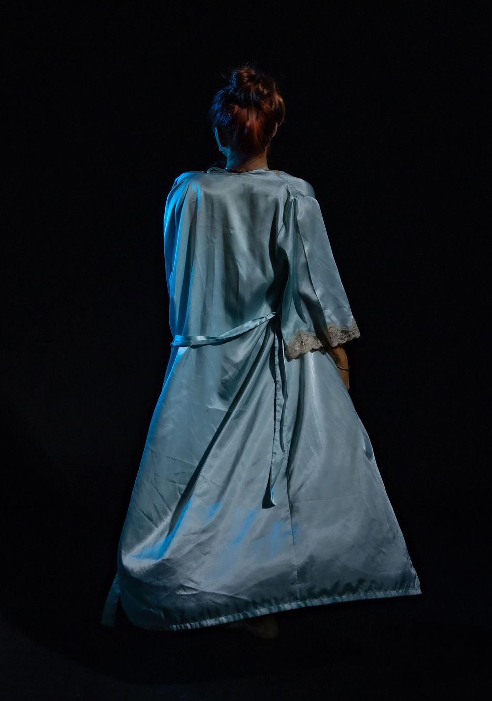 Dramatic rear view silhouette with billowing blue-tinted fabric against black background.