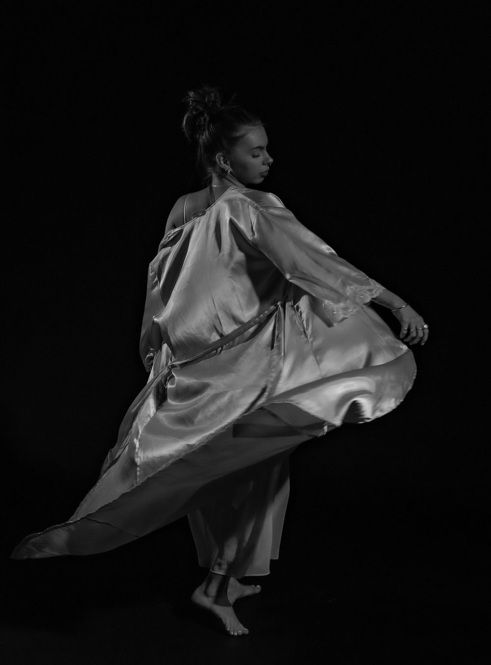 Black and white artistic fashion photo capturing flowing dress movement against dark backdrop.