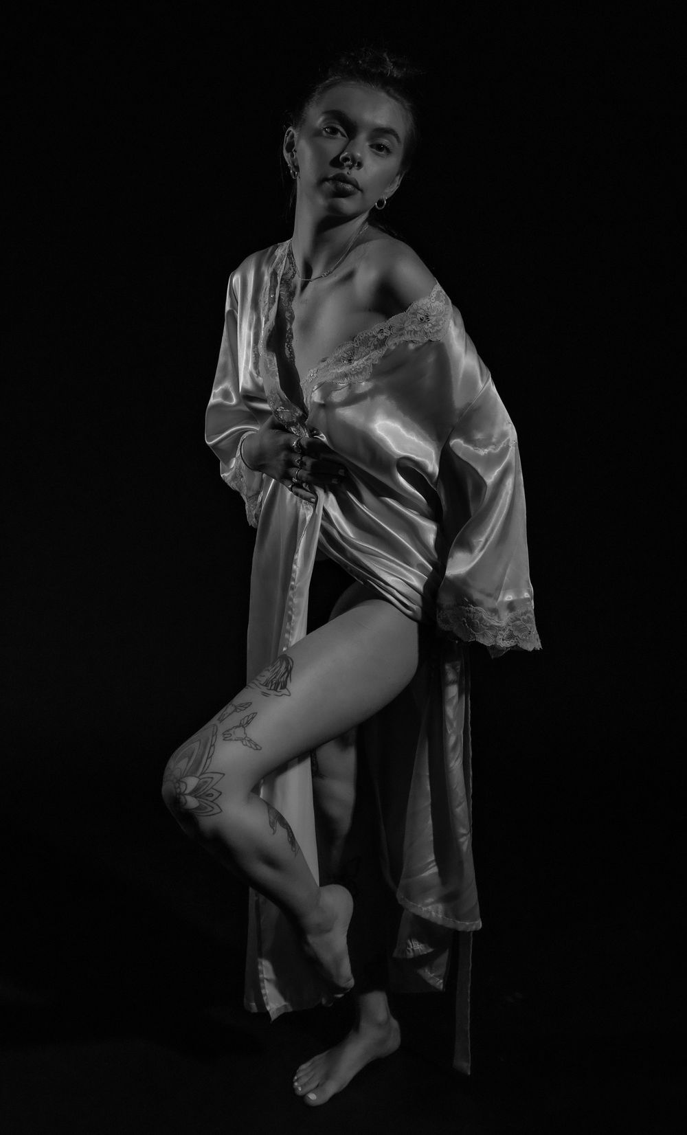 Monochrome artistic portrait showing tattoo details and silk robe in dramatic lighting.