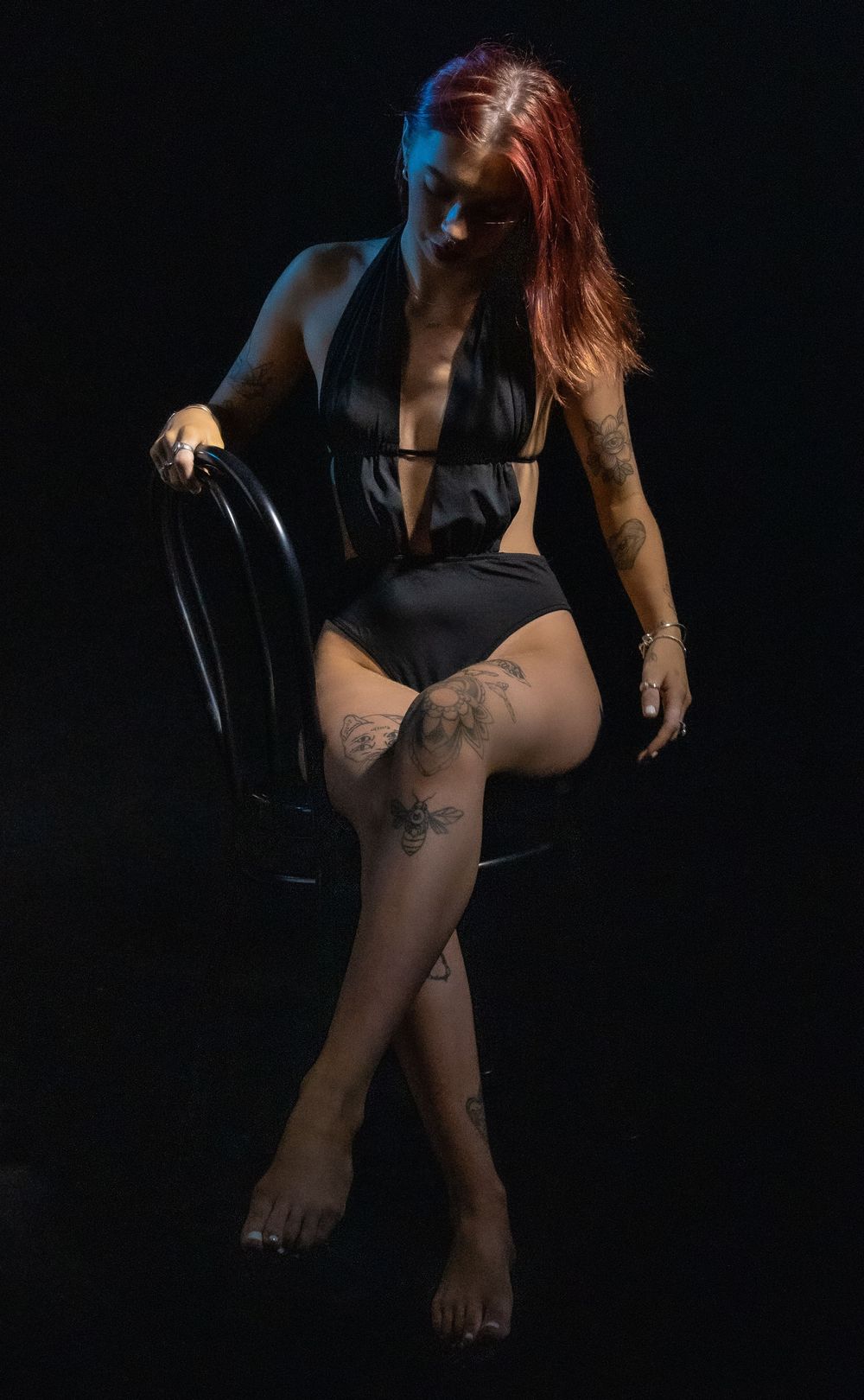 Dramatic portrait with red and blue lighting featuring black swimwear and artistic tattoos.