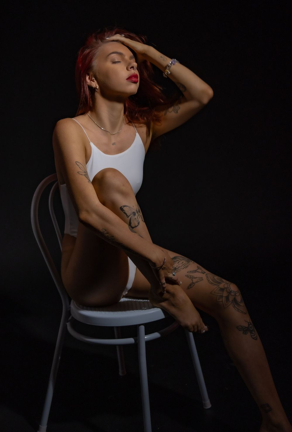 Moody studio photography with dramatic shadows showing seated figure in white against black backdrop.