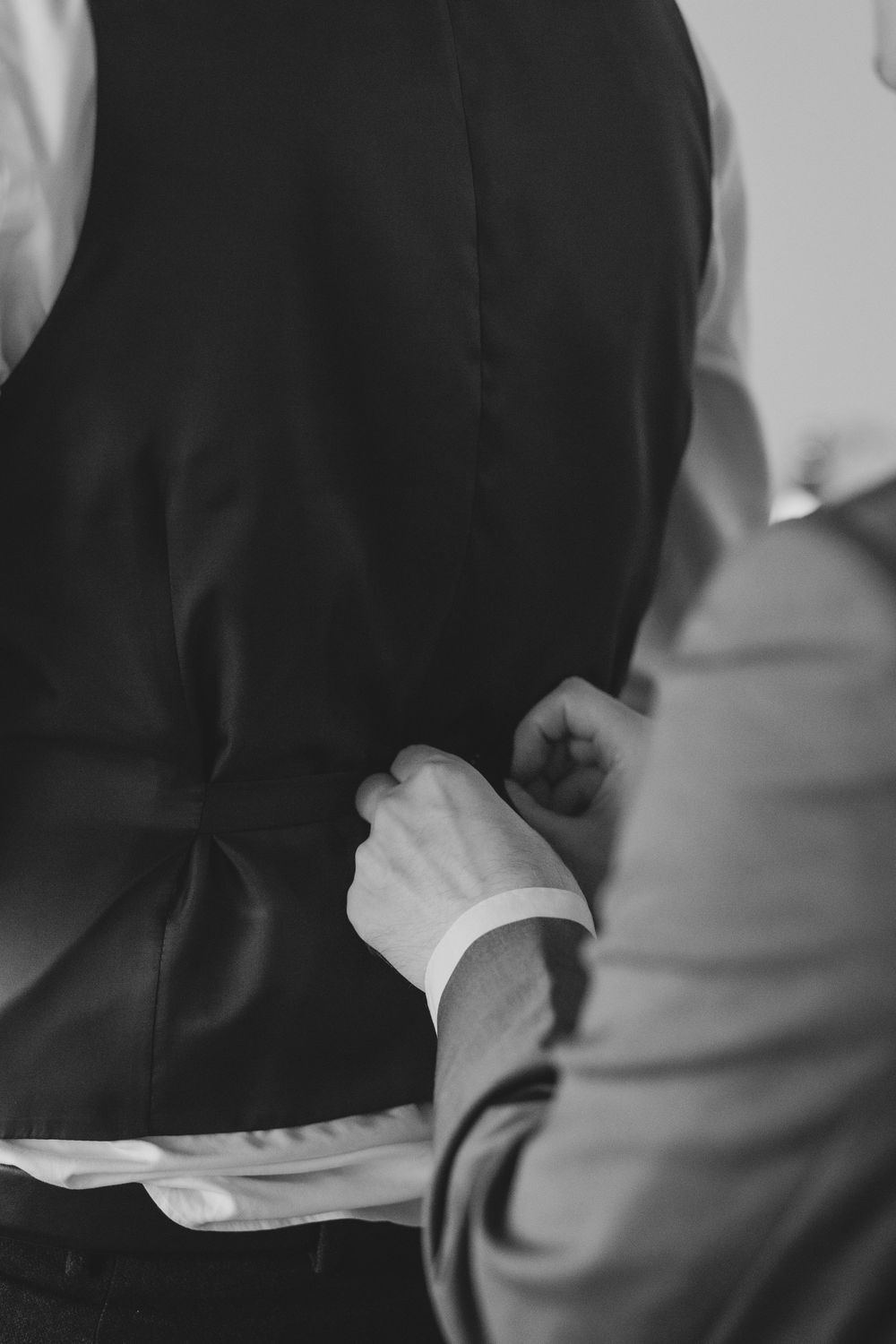 Close-up black and white photo of hands adjusting a suit vest and cuff during formal dressing.