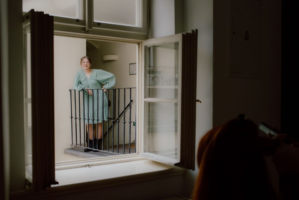 A person stands on an interior balcony with white walls and glass doors, dramatically lit in a moody atmosphere.