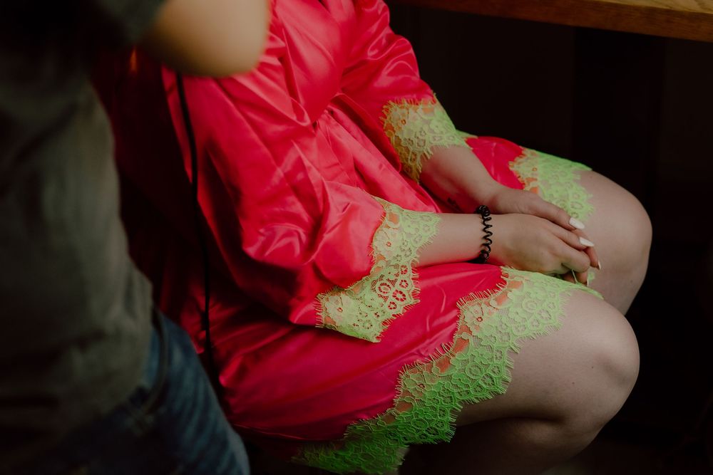 A person wearing a vibrant red dress with neon green lace trim sits with hands folded in their lap.