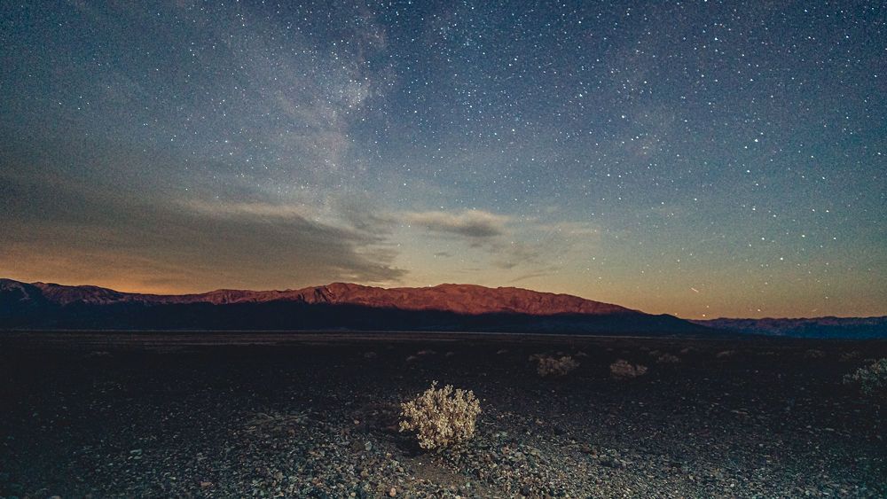 Beautiful night sky with Milky Way over desert landscape with mountains and shrubs in Death Valley National Park.