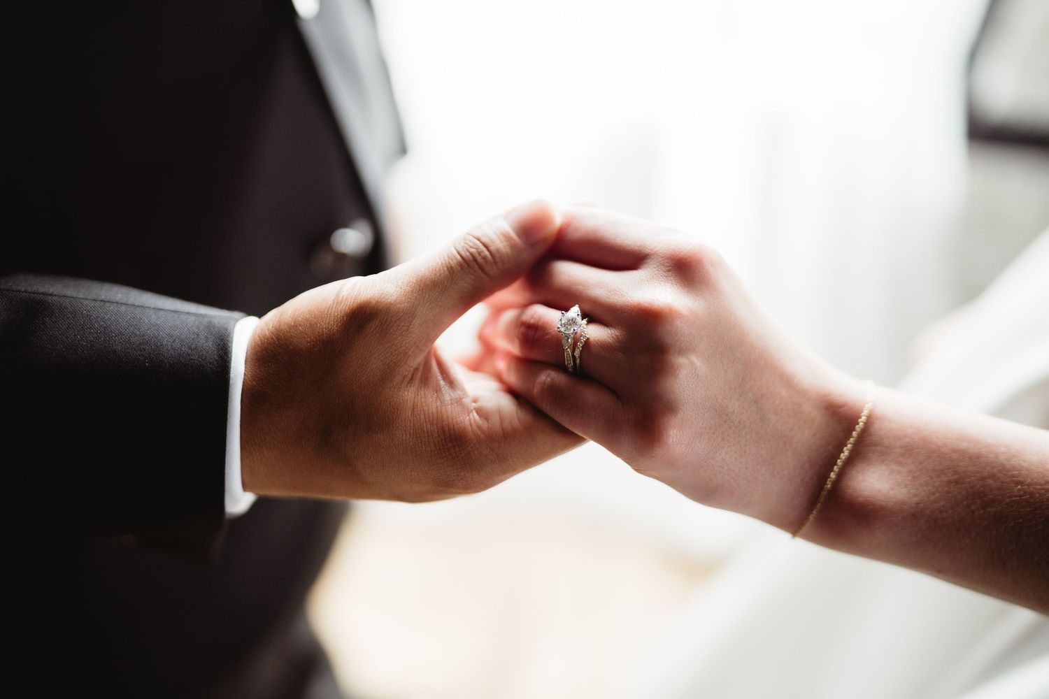 Close-up of two hands touching tenderly during a wedding ceremony, with one wearing a wedding ring.