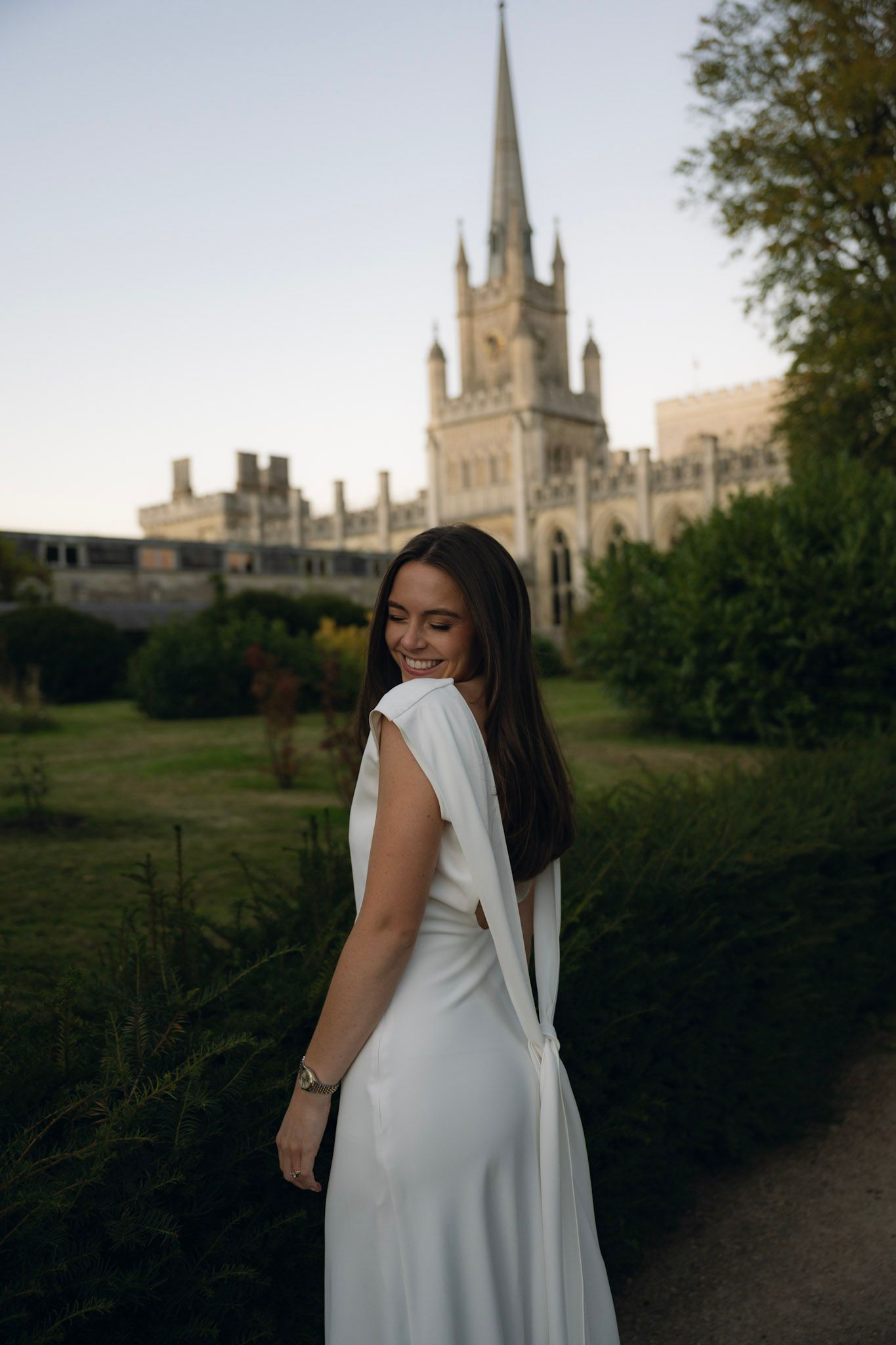 White dress flowing against the backdrop of a gothic cathedral spire at sunset.