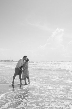 Romantic couple standing in ocean waves during a beach photoshoot.
