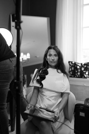 Black and white portrait of someone in a white outfit sitting by a window.