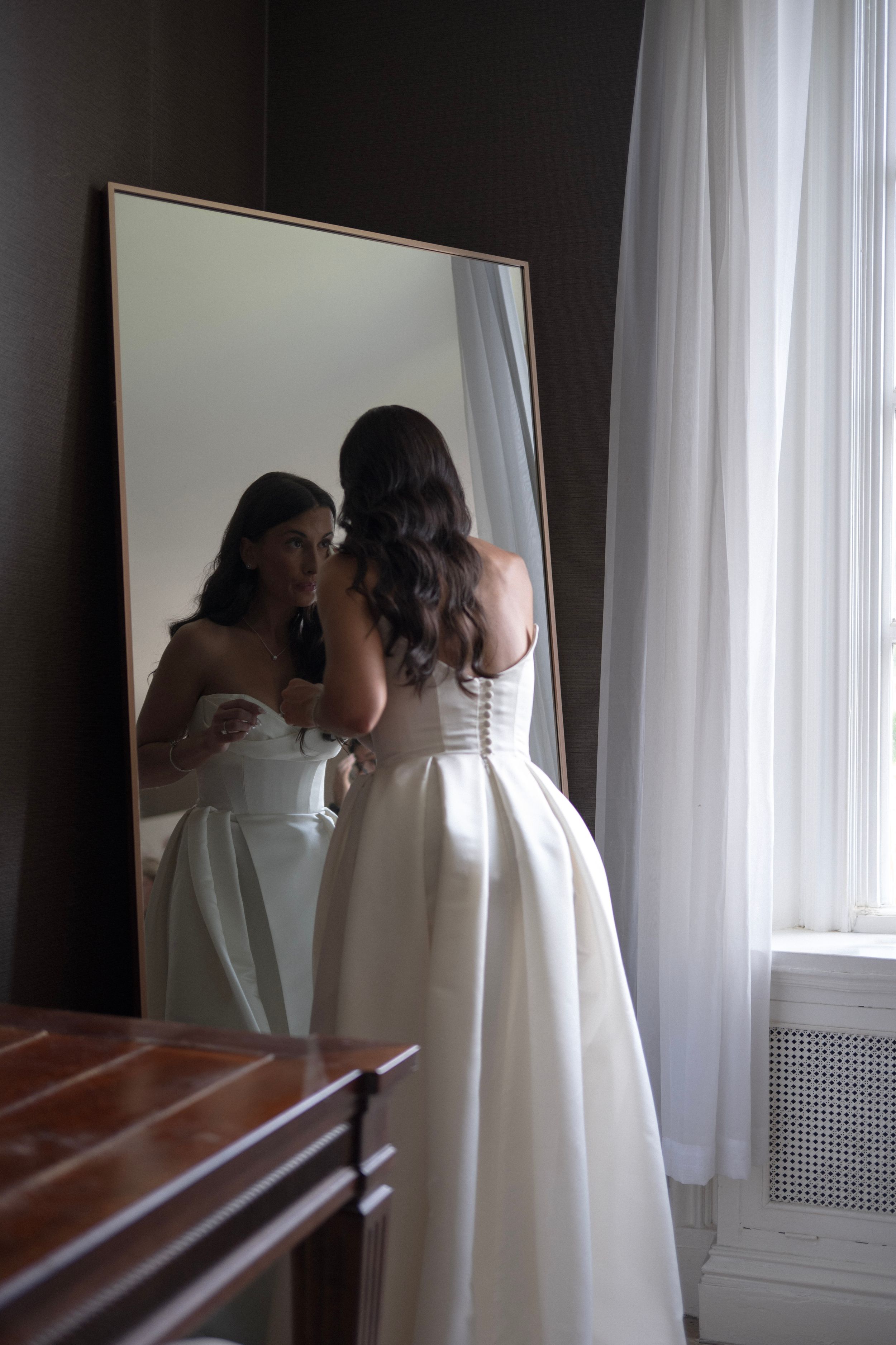 Wedding dress preparations in a sunlit room with mirrors.