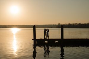 Couple silhouetted on a wooden dock at golden sunset over calm lake waters.