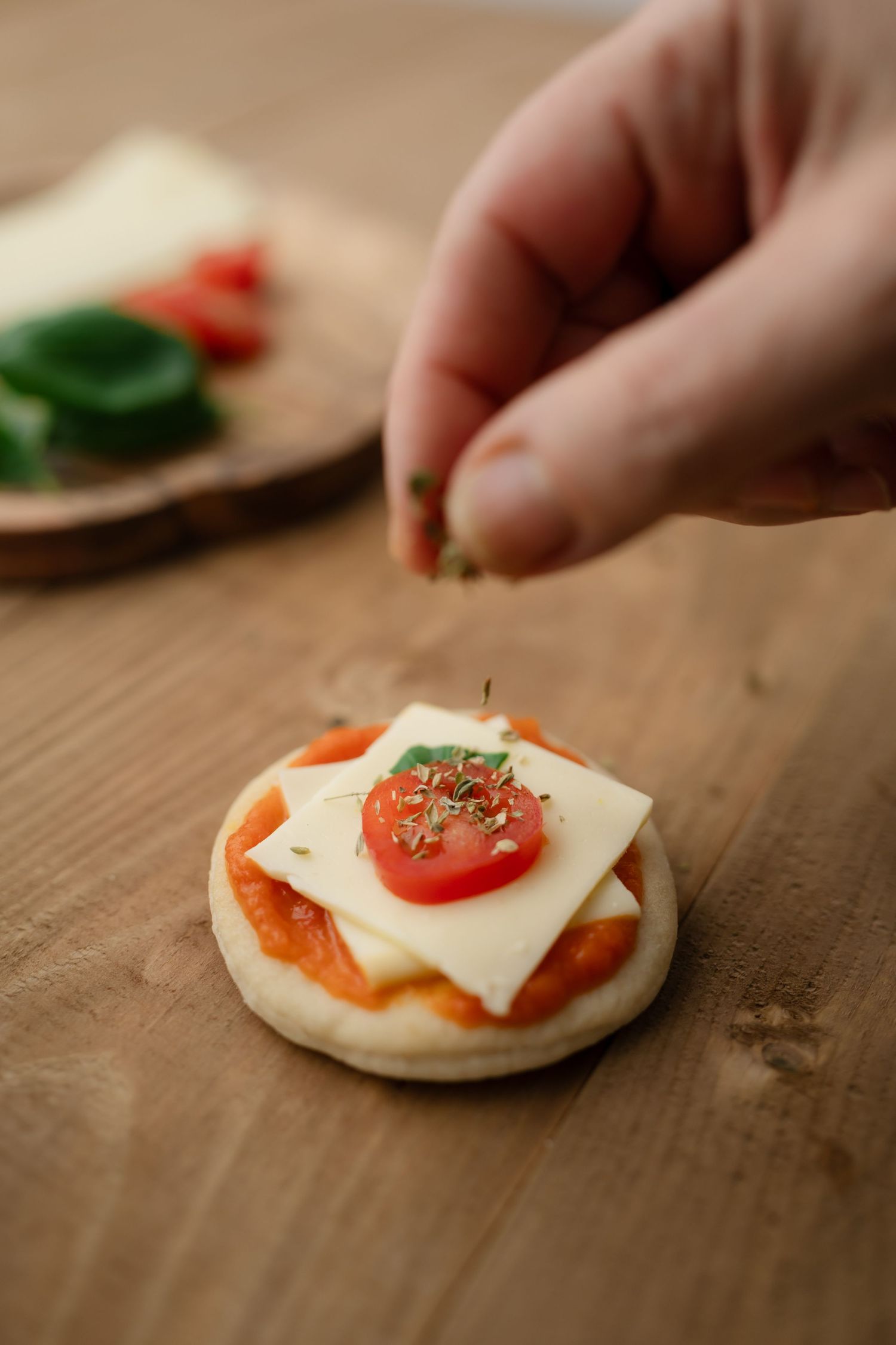 Close-up of assembling a small sandwich with cheese, tomato and herbs on a wooden surface.