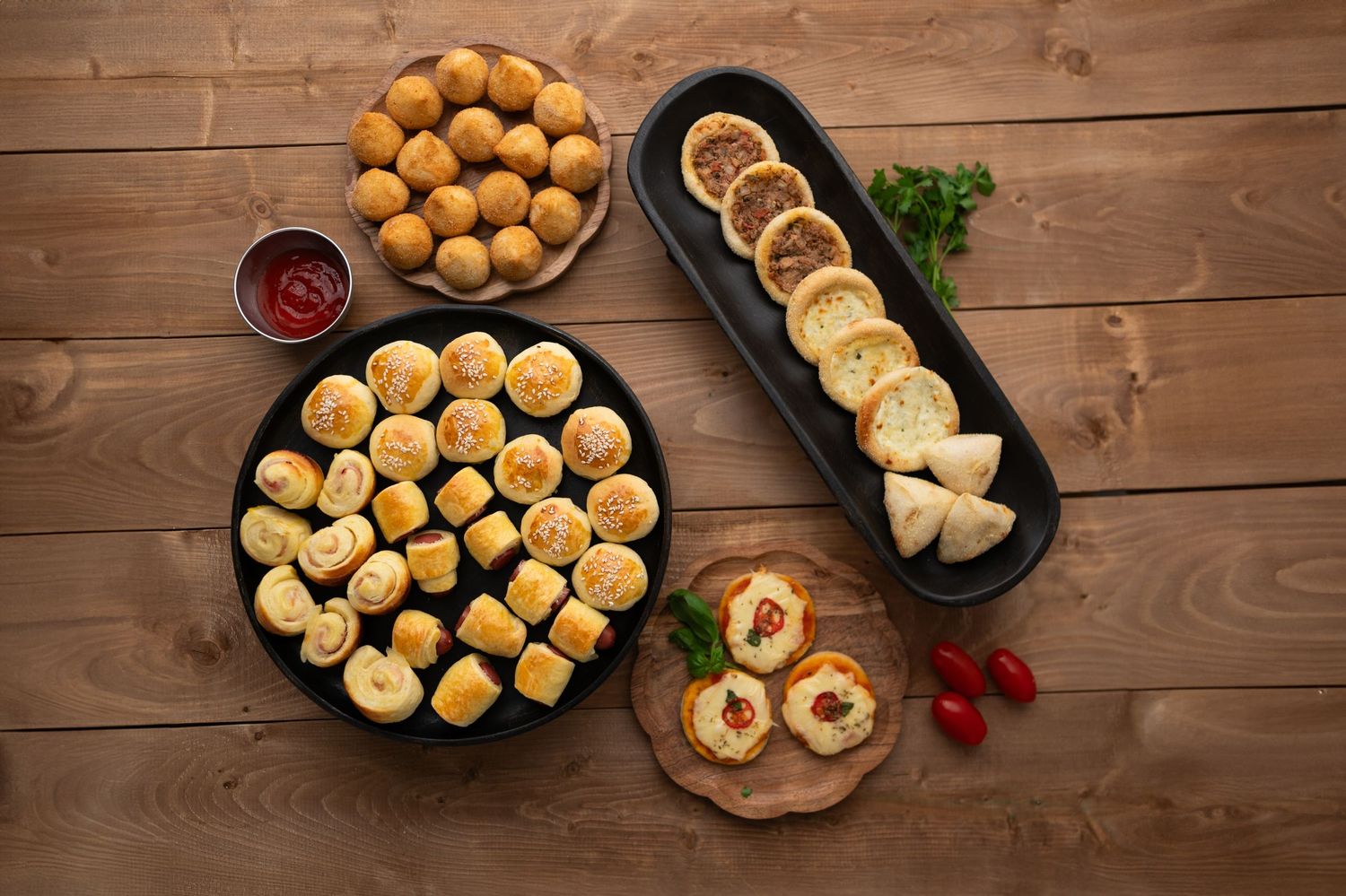 Overhead view of platters filled with baked goods, served with dipping sauce and garnishes.