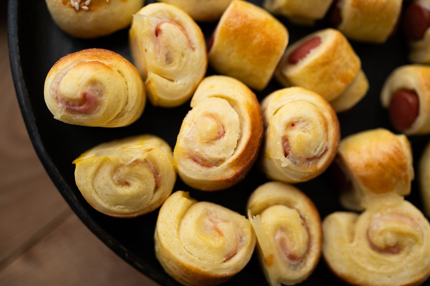 Close-up of spiral-shaped pastry rolls with ham filling in a cast iron pan.