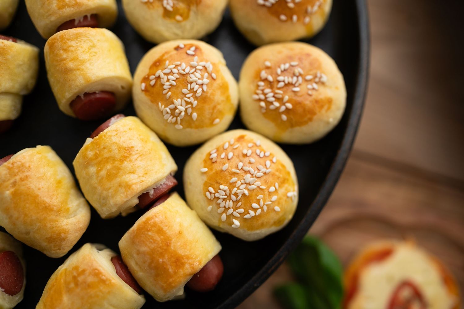 Golden brown dinner rolls topped with sesame seeds arranged in a black serving dish.
