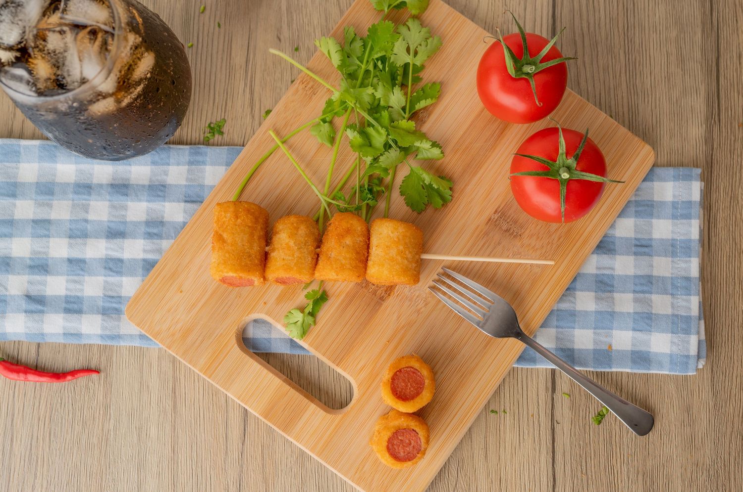 Wooden cutting board with stuffed breaded snacks, tomatoes, and herbs in rustic setting.