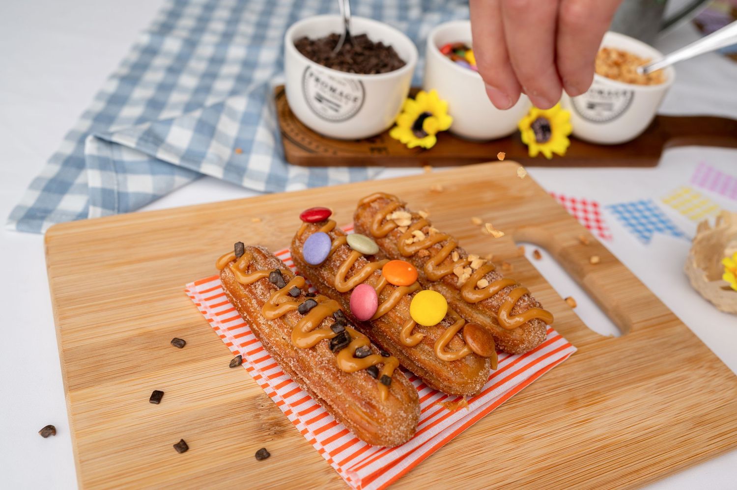 Wooden serving board with snacks and colorful decorative elements on checkered tablecloth.