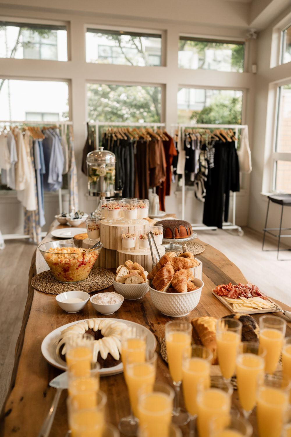 A buffet spread with snacks and orange drinks displayed on wooden tables with clothing racks in background.