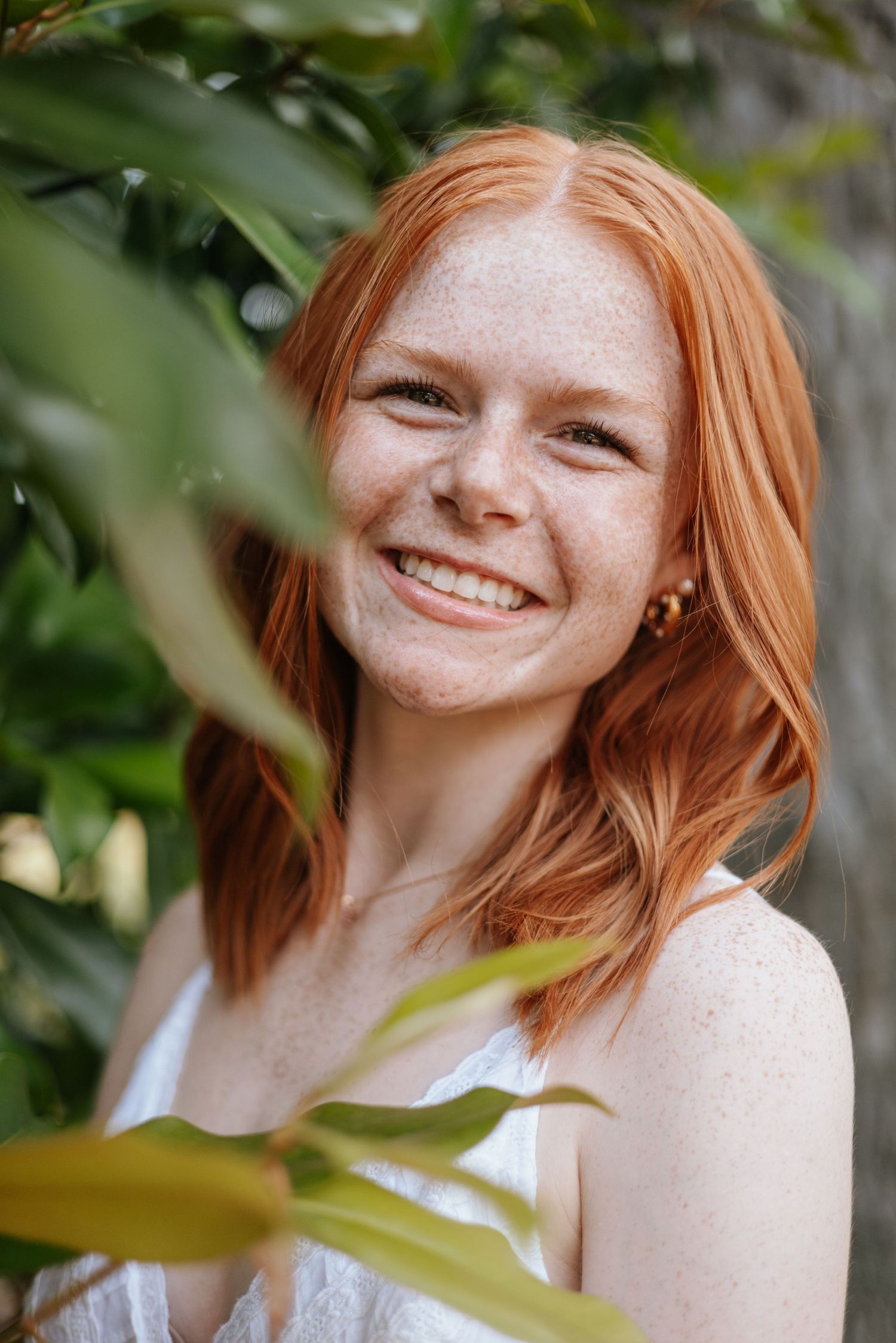 Candid portraits of redhead woman smiling among green leaves.